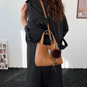 Détail du sac seau en cuir grainé marron avec fermoir argenté et pompon décoratif doux