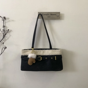 Close-up of black shoulder bag with white faux shearling trim and brown glove pendant