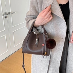 Détail du sac seau en cuir marron foncé avec fermoir argenté et pompon violet décoratif
