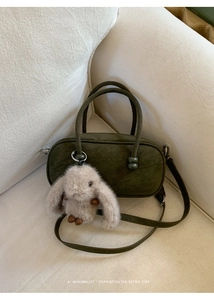 Olive green nubuck Boston bag featuring a plush bunny charm on a soft white sofa