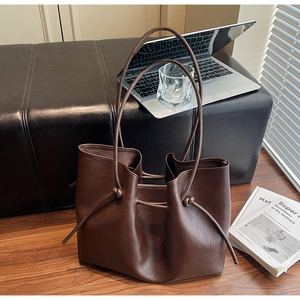 Detail of dark brown tote bag with knot strap on leather bench with a laptop