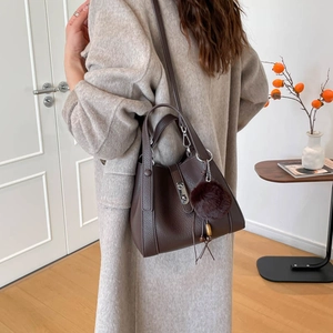 Détail du sac seau en cuir grainé marron foncé avec boucle métal et pompon en fourrure