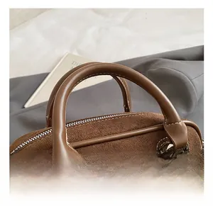 Detail of dark brown suede baguette bag with contrast stitching and silver metal rings