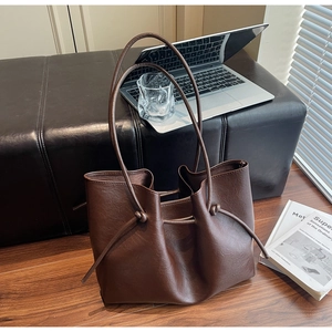 Detailed view of dark brown tote bag with decorative knot handles on a wooden floor