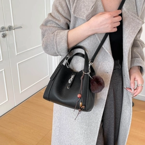 Détail d'un sac seau noir en cuir grainé avec pompon en fourrure et bijoux de sac