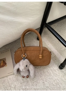 Brown Boston handbag with wooden bead details and a plush bunny charm on a rug