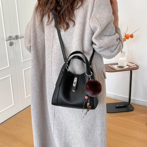 Détail du sac seau en cuir grainé noir avec fermoir métal et pompon violet soyeux