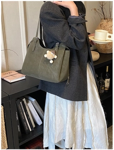 Detail of dark green leather tote bag with plush charm on vintage wooden background