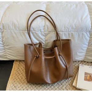 Detail of a brown tote bag with slim shoulder straps and side knot decoration on a soft rug
