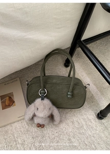 Olive green Boston bag with plush rabbit charm and cylindrical handles in a retro setting