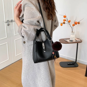 Détail du sac seau noir en cuir grainé avec pompon rouge et fermoir rotatif en métal argenté