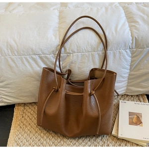 Detail of a brown leather tote bag with drawstring closure on a lifestyle background