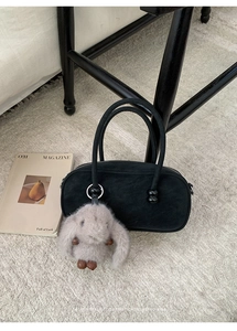 Detail of black suede Boston bag with a fuzzy grey rabbit charm on textured carpet
