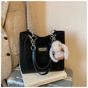 Macro detail of black suede tote bag with silver chain strap and plush bunny charm