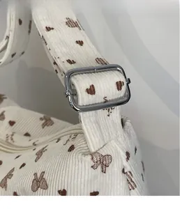 Détail de boucle en métal argenté sur sac en velours beige à motifs de cœurs