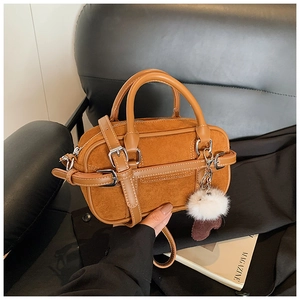 Detailed shot of caramel suede and leather Boston bag with plush ball charm and top handles