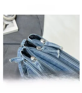 Detail of blue denim shoulder bag showing three metal zippers with fabric pullers