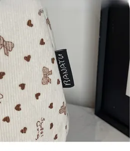 Détail du sac fourre-tout en velours blanc avec motifs cœurs et nœuds et étiquette