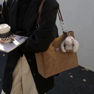 Detail of brown tote bag featuring metal chain straps and fluffy rabbit charm accessory