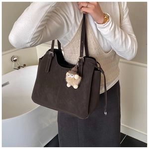 Detail of dark brown tote bag with suede texture and cute fuzzy monster pendant charm