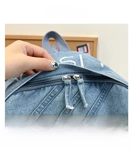 Detail view of smooth dual metal zippers on a blue denim backpack with logo prints