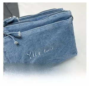 Detail of blue denim crossbody bag featuring white embroidery and distressed raw edges