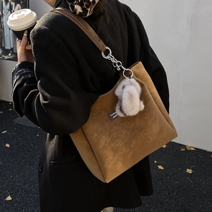 Detail of brown suede tote bag with chain strap and cute rabbit pendant on a black coat