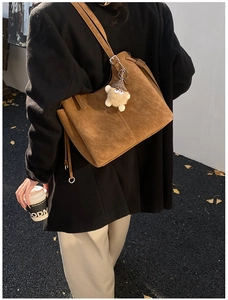 Detail of brown suede tote bag featuring a decorative plush acorn charm and metal hardware