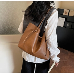Detailed side view of a large brown leather tote bag worn by a model in a minimalist room