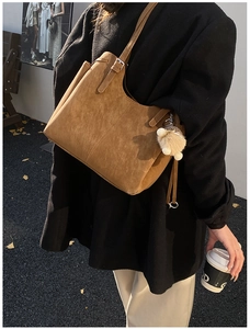 Brown faux suede tote bag with plush ball charm shown in a street style setting