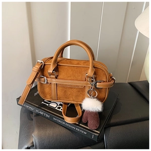 Close-up of brown suede Boston bag on books with leather straps and glove charm