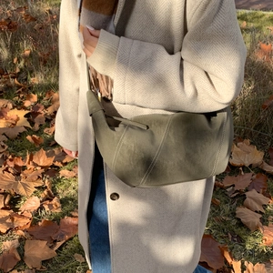 Détail du sac demi-lune vert foncé avec surpiqûres blanches sur un manteau en laine beige