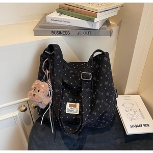Detail of black corduroy tote bag with heart prints and a plush bear charm