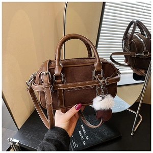 Macro detail of brown suede Boston bag with white stitching and plush ball charm