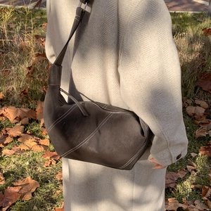 Détail du sac bandoulière en daim marron foncé avec surpiqûres blanches en décor automnal