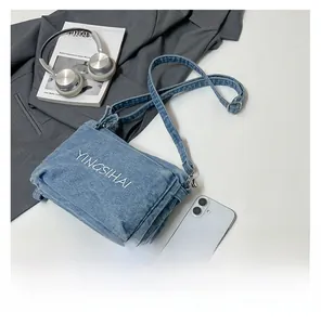 Detail view of denim crossbody bag with white embroidery and multi-layer zipper pockets