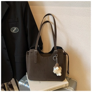 Detail of dark brown tote bag with drawstring sides, plush charm and silver metal hardware
