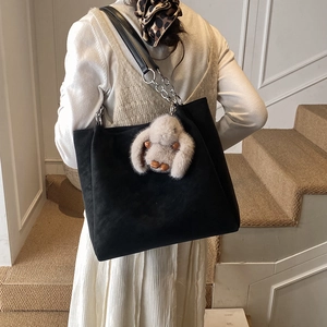 Detail of black suede tote bag with metal chain strap and cute beige rabbit charm