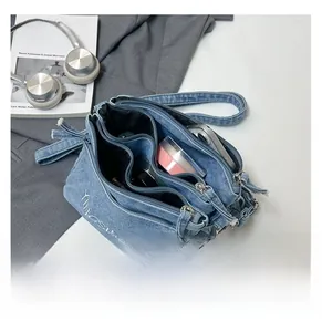 Detailed view of blue denim shoulder bag with multiple zippers and large capacity