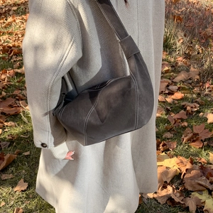 Détail du sac à bandoulière en cuir mat gris foncé avec surpiqûres blanches sur un manteau