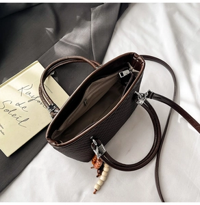 Detail of dark brown woven tote bag with dual handles, shoulder strap and beaded charm
