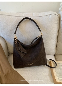 Detail of a dark brown hobo bag with gold logo, mini pouch, and soft suede texture