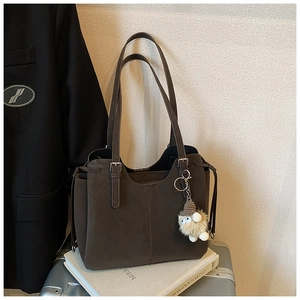 Detail of dark brown suede tote bag with plush monster charm and leather drawstring