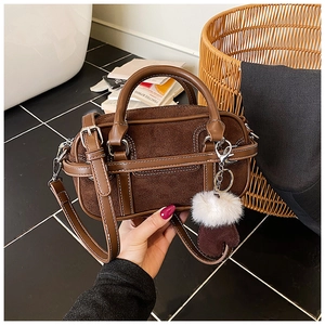 Detailed close-up of a brown Boston bag with leather stitching and a plush pompom charm