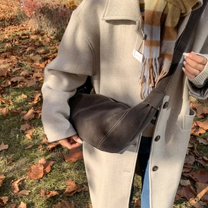 Détail d'un sac bandoulière en daim marron foncé avec surpiqûres sur un manteau d'hiver