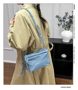 Close-up of blue denim crossbody bag with white letter embroidery worn by a model