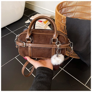Detail of brown suede Boston bag with leather trim and decorative white pompom charm