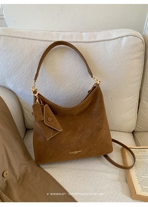 Detail shot of a brown vintage tote bag with small matching pouch and brand logo on a sofa