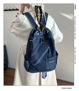 Detail of vintage blue denim backpack with white embroidery and multi-pocket design