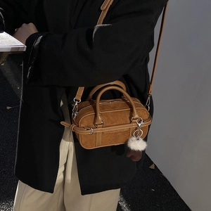 Detail of caramel brown suede Boston bag with fuzzy pom-pom charm and strap